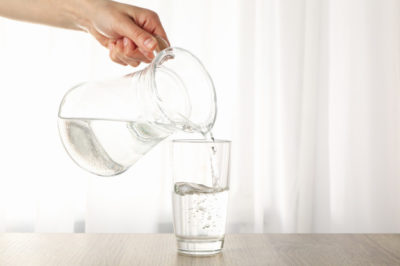 pouring-purified-fresh-water-from-jug-glass-wooden-table_185193-14605